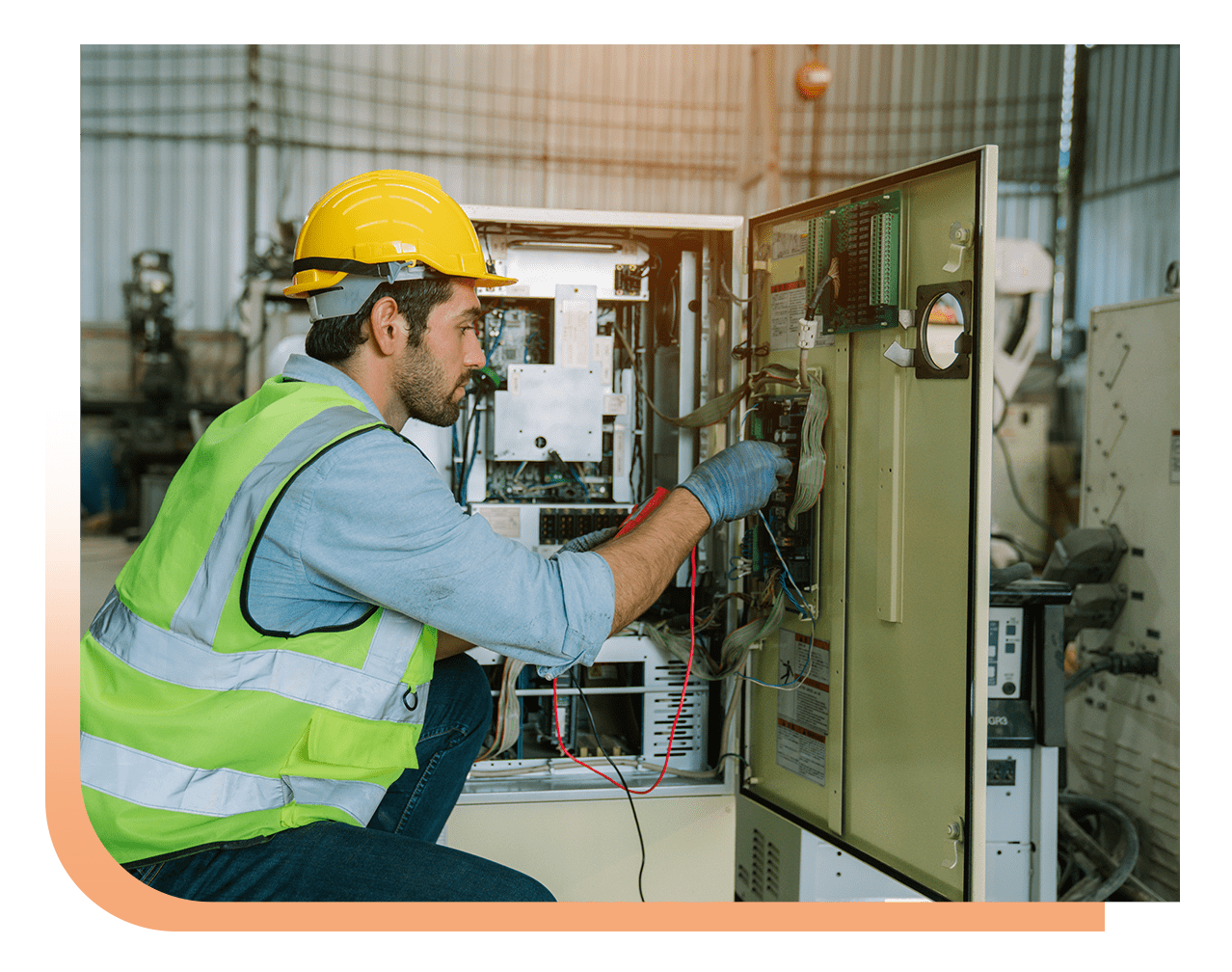 Male technician in a yellow hard hat and high‑visibility vest repairing an open industrial control panel.