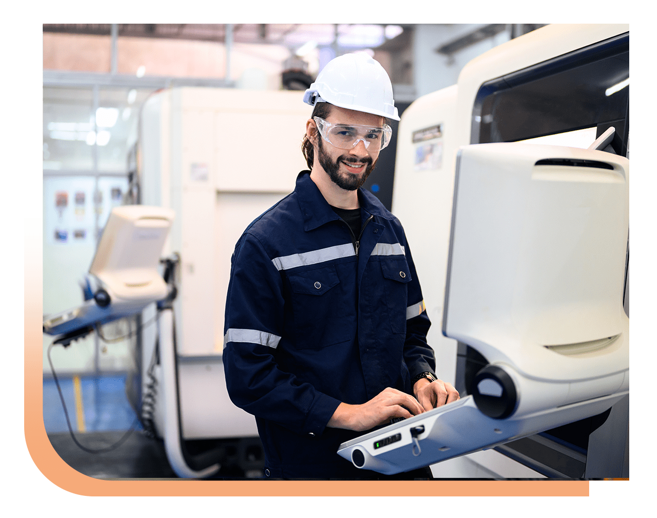 Man in hard hat and safety glasses operates a large industrial machine at a workshop, typing on a control panel