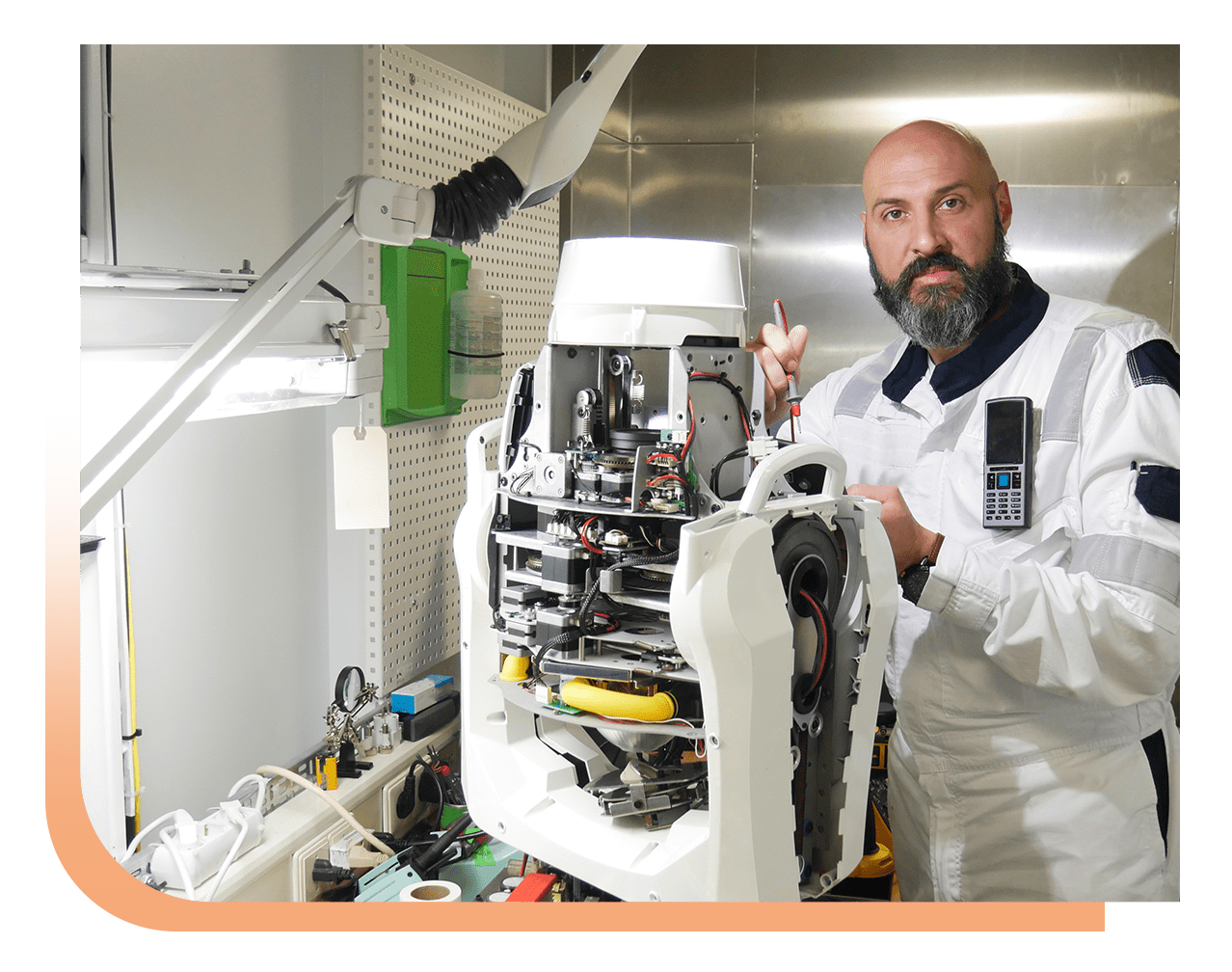 Bearded technician in a white suit repairing a disassembled white robotic device in a lab setting